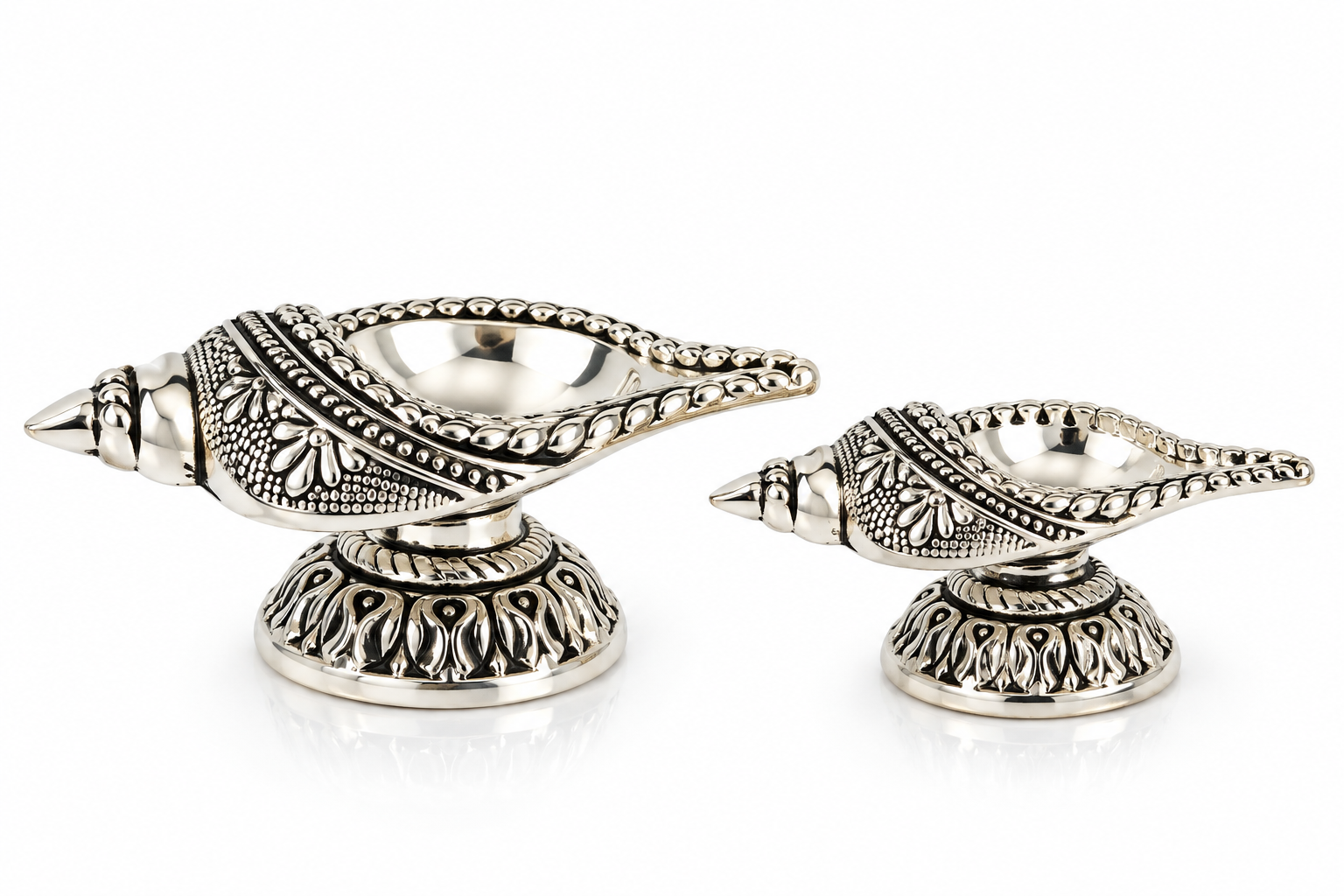 Pair of Mohnaa Jyotika sterling silver ornate diyas displayed in two sizes, featuring decorative elongated bowls and sculpted pedestal bases.