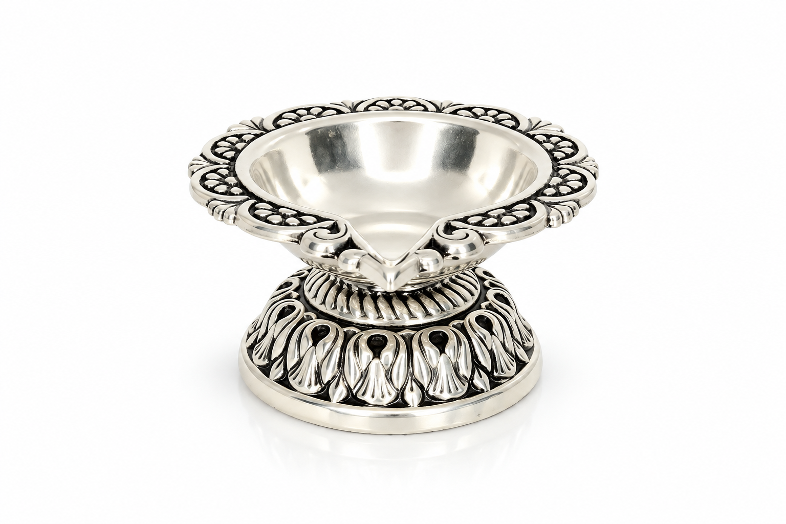 Mohnaa Shreepad 925 sterling silver decorative diya featuring an ornate scalloped rim, polished bowl, and intricately detailed pedestal base on a white background.

