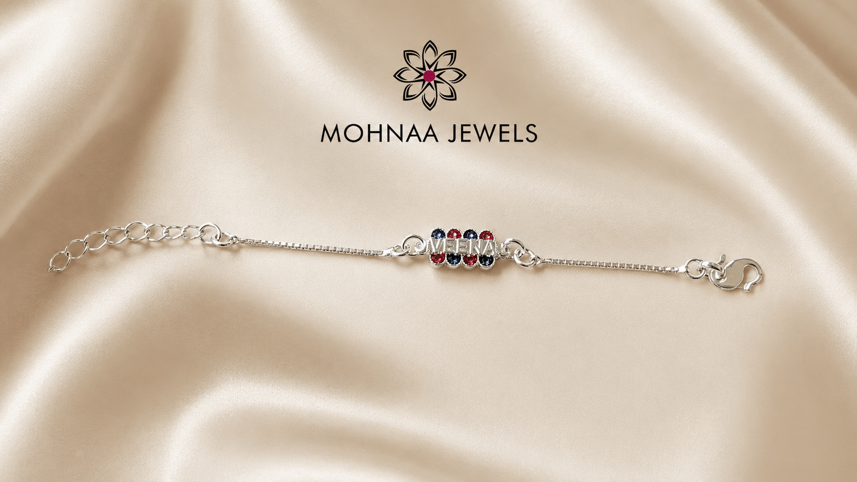 "Veera Silver Bracelet Rakhi featuring a personalized name charm with red and blue gemstone accents on an adjustable 925 sterling silver chain, displayed on a luxury satin background."