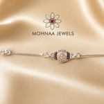 "Om 925 Silver Rakhi featuring a sacred Om symbol with sparkling stone embellishments on an adjustable sterling silver chain, elegantly displayed on a luxury satin background by Mohnaa Jewels."